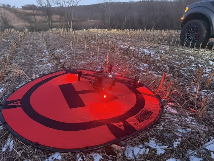 Search drone lit red on a landing pad in a snowy cornfield at dusk